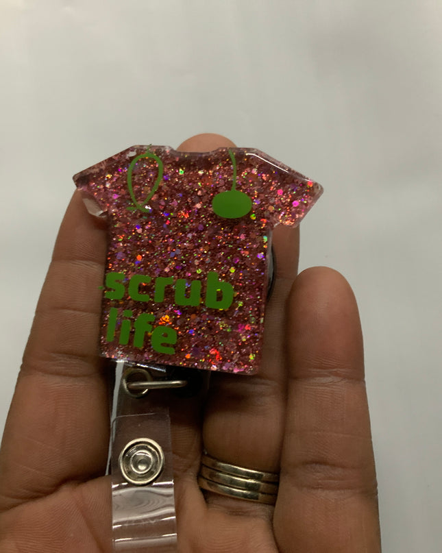 Bling Treasures small scrub top shaped badge reel with the words Scrub Life written on it are fashionable. It comes in variety of colors, red, black, blue, pink, silver & purple.  Length 2 inches width1 1/2 inches Beyond Medwear Apparel